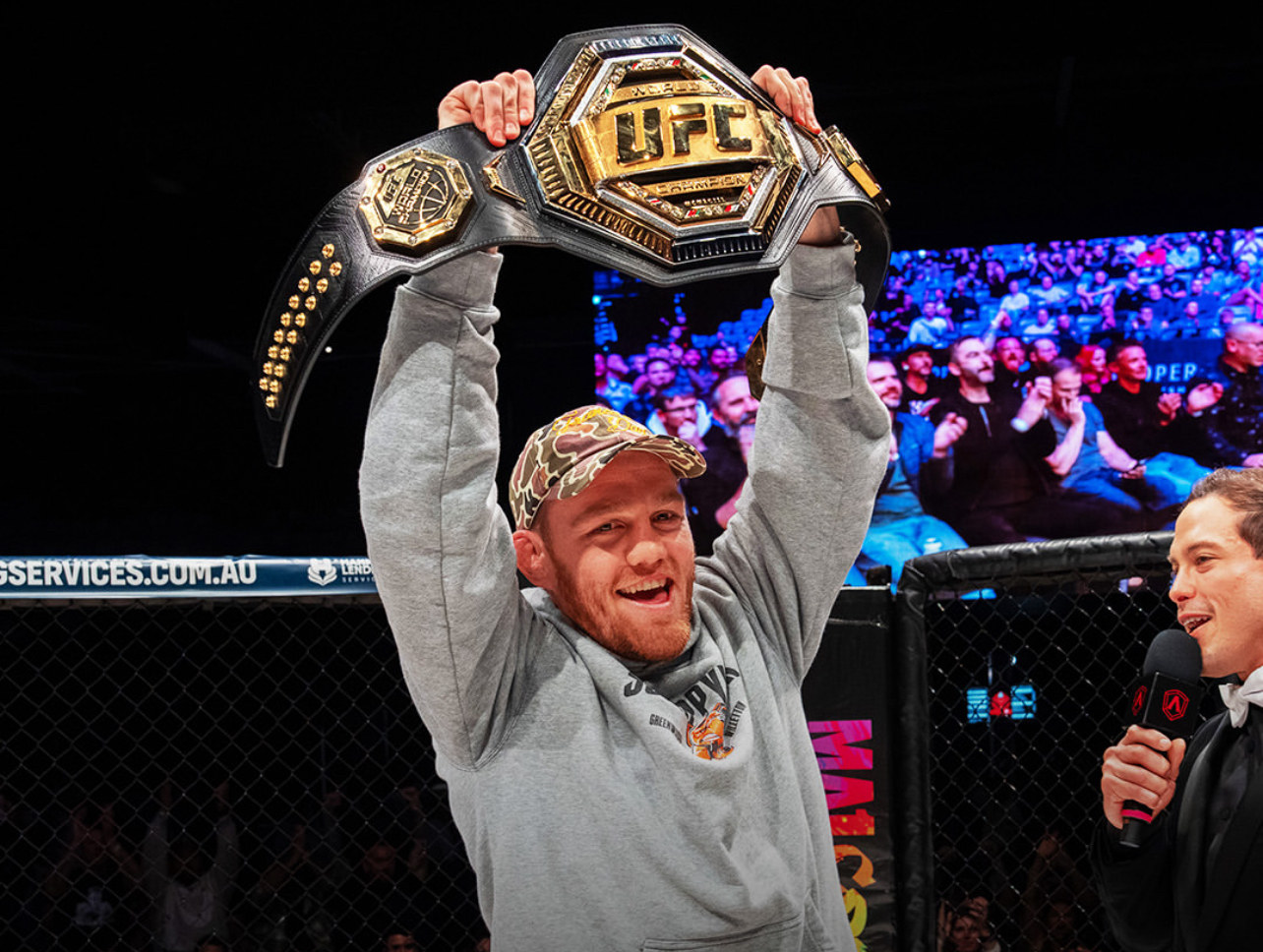 Person holding UFC championship belt inside octagon at Perth UFC event