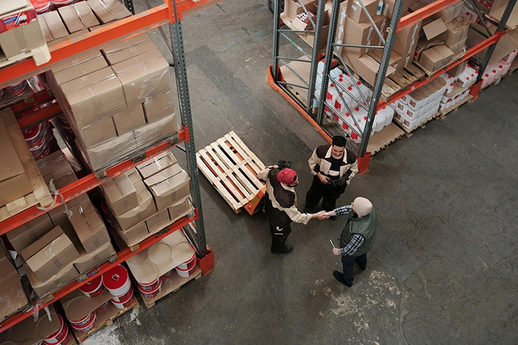Warehouse workers coordinating in a wholesale cleaning supplies storage area with shelves stocked with products