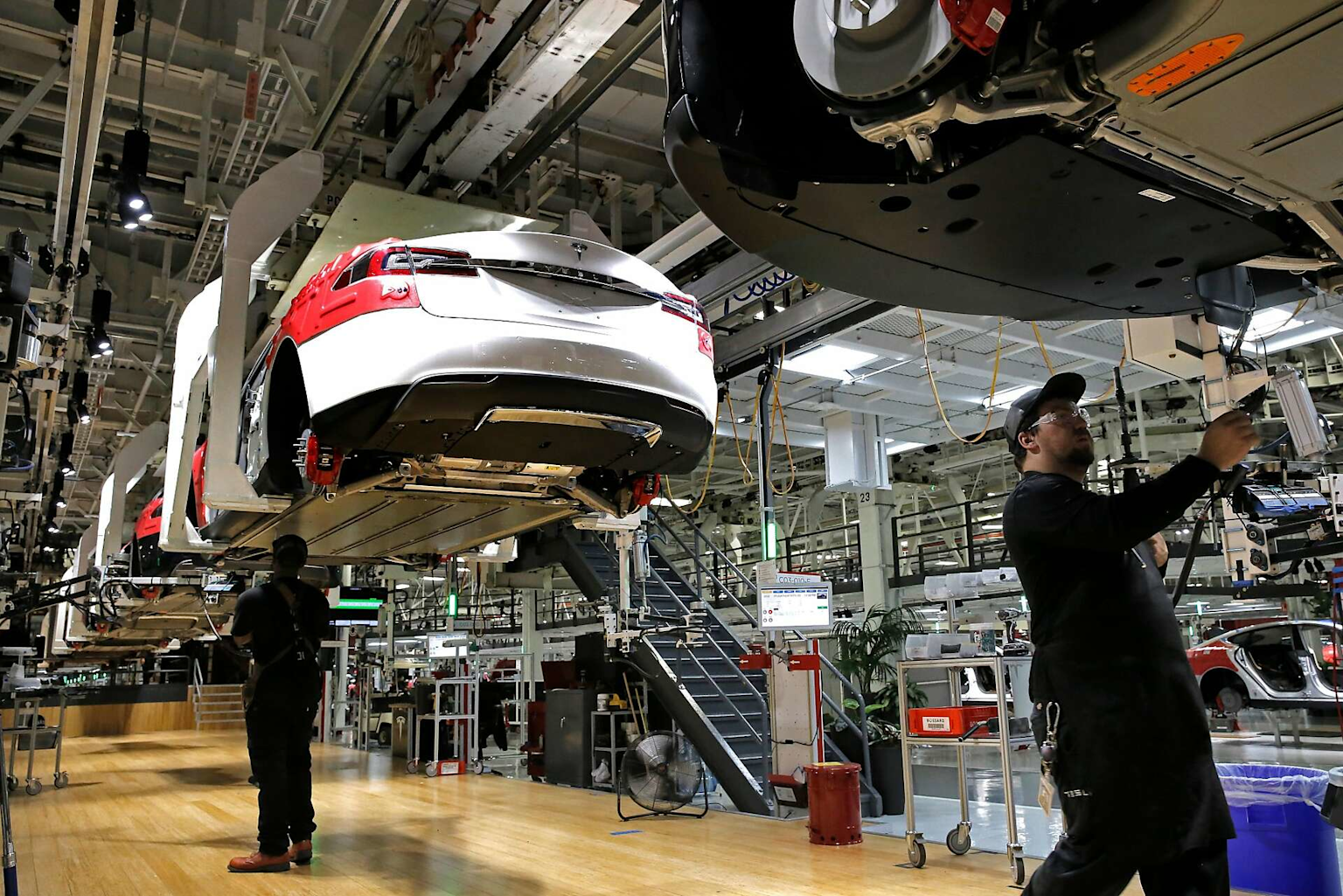 Tesla factory assembly line showing cars in production and workers engaged in the manufacturing process