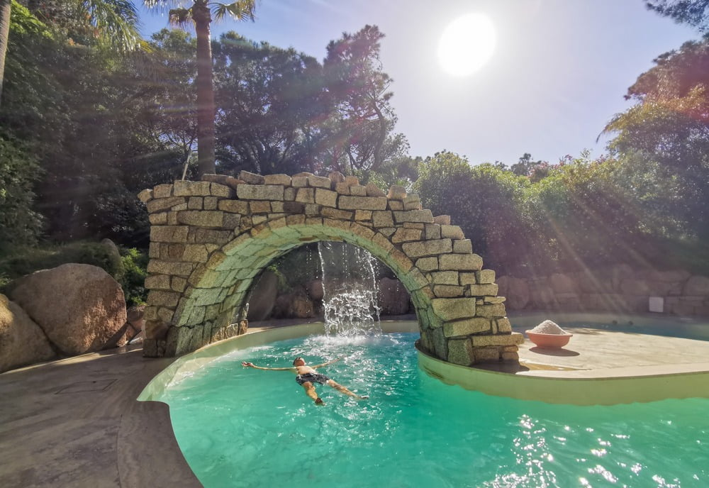 Luxurious outdoor spa pool with cascading waterfall at a Sardinian wellness retreat under bright sunlight