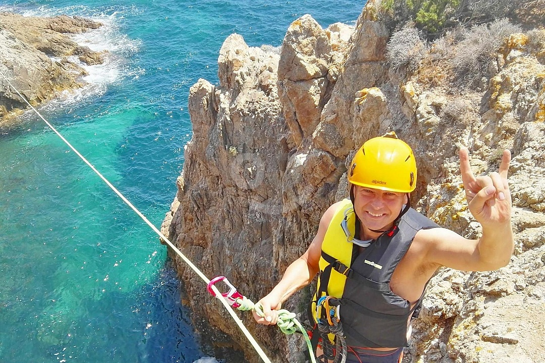 A coasteering adventurer in safety gear explores the rugged cliffs and clear waters of Sardinia, Italy