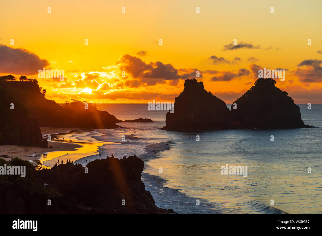 Sunset view of the Morro Dois Irmãos rock formations at Fernando de Noronha, Brazil, illuminating the ocean with golden hues