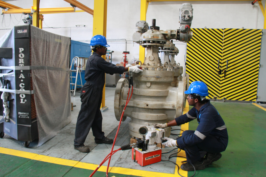 Technicians performing maintenance and inspection on a large industrial valve using hydraulic tools in an industrial facility