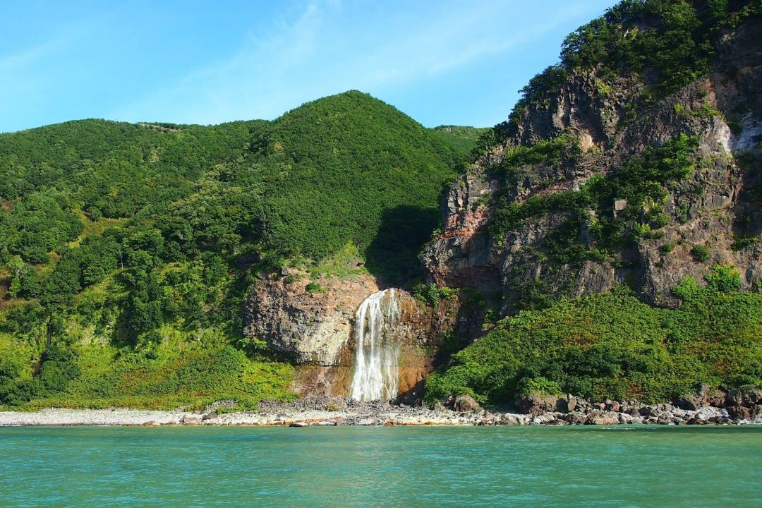 Secluded waterfall and lush green cliffs by turquoise coastal waters on a clear day