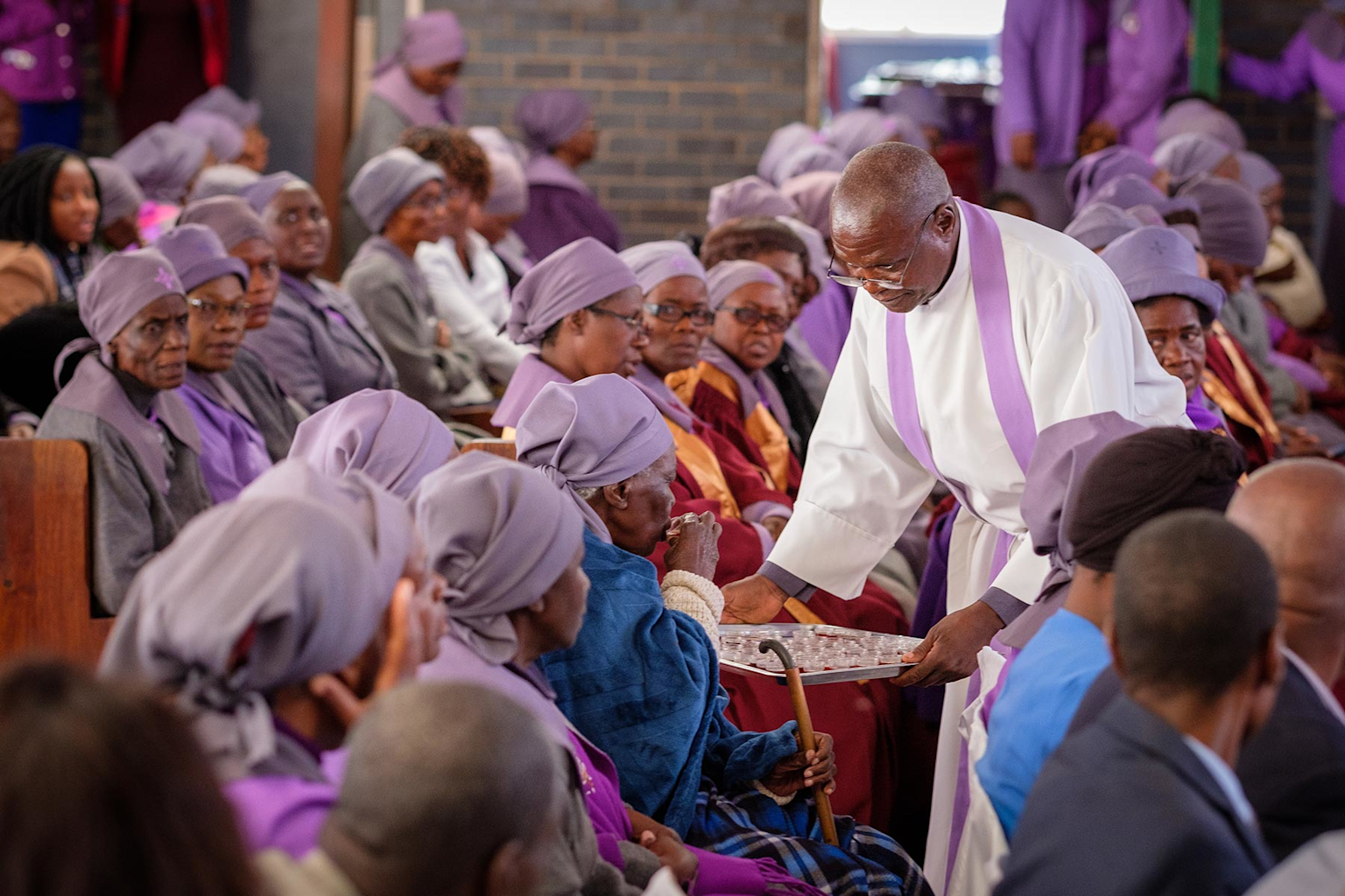 African religious ceremony with a priest administering communion to elderly congregants in a church setting