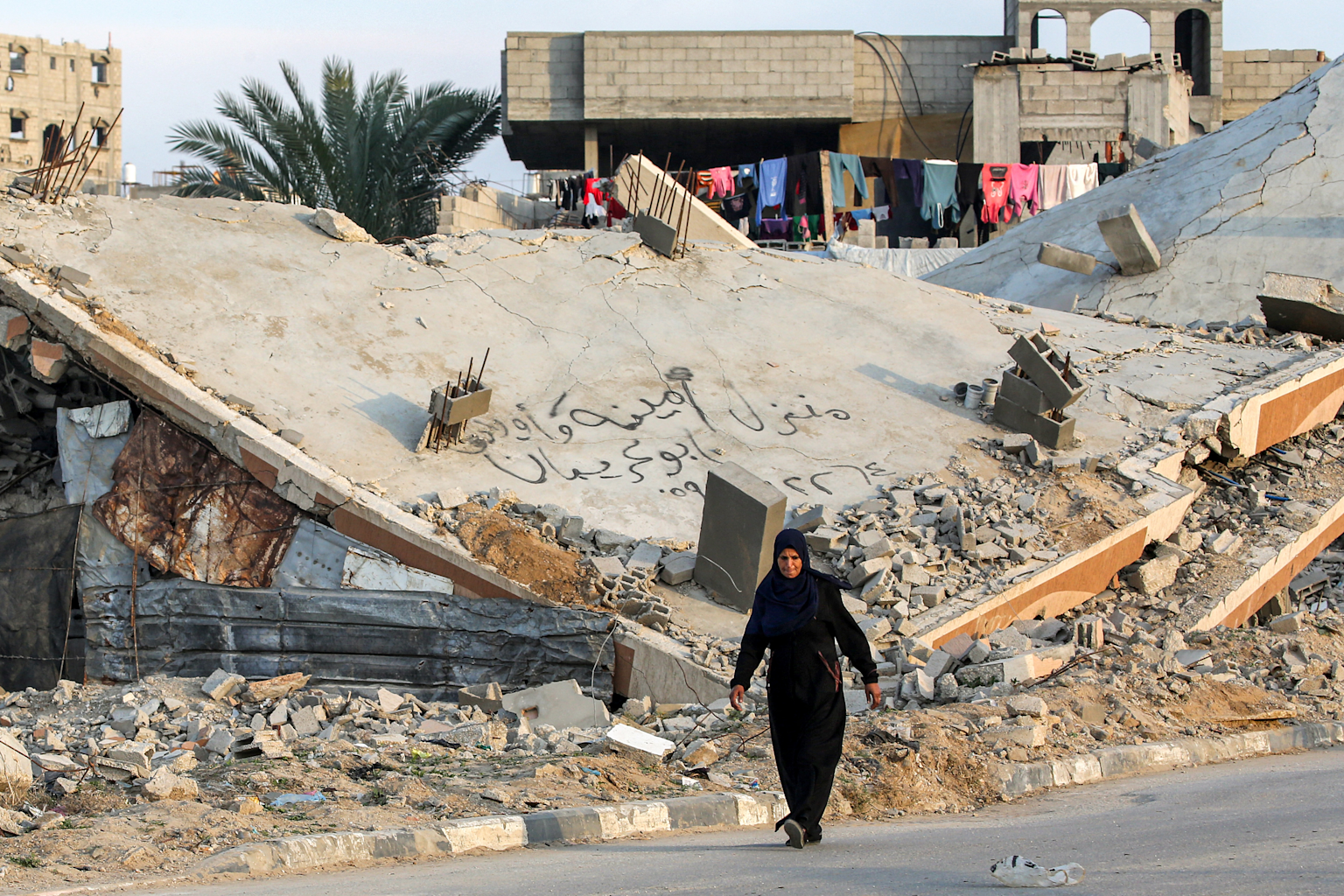 A person walks past a collapsed building amid rubble in Gaza, illustrating the extent of destruction and impact on civilian life