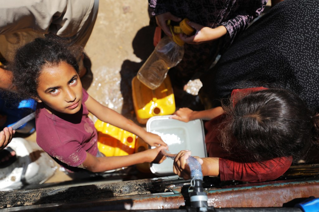 Children and adults in Gaza collect scarce clean water from a pipe into containers amid harsh conditions
