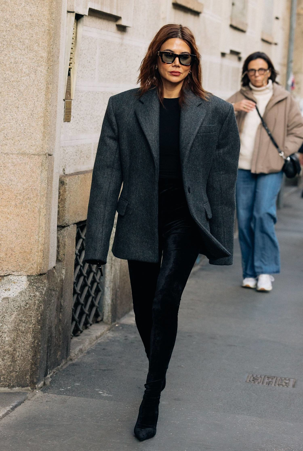 Woman wearing a dark gray oversized wool blazer layered over a black top with black leggings and boots in a winter street style outfit.
