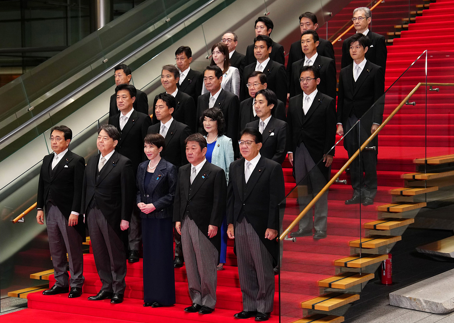 Group photo of Japanese politicians in formal attire on a red-carpeted staircase, likely representing a cabinet or official government gathering