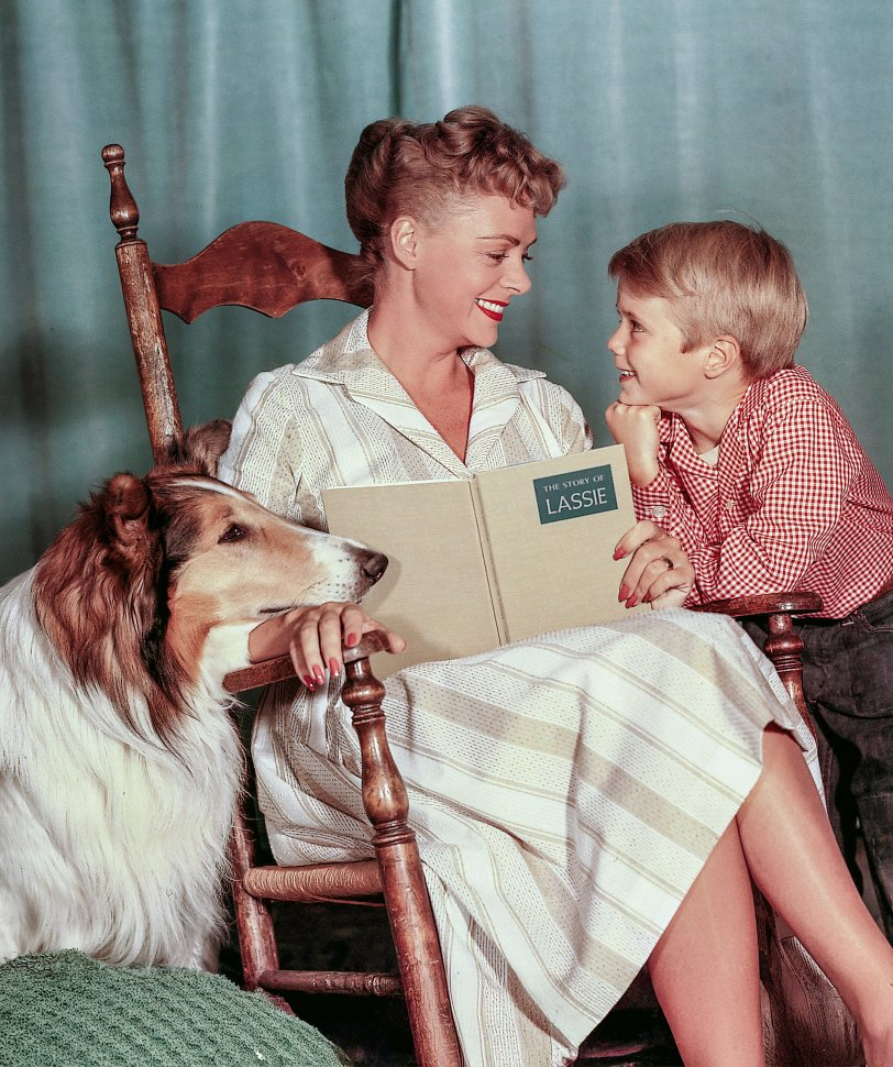 A woman reading a book with a boy and a dog beside her in a vintage setting
