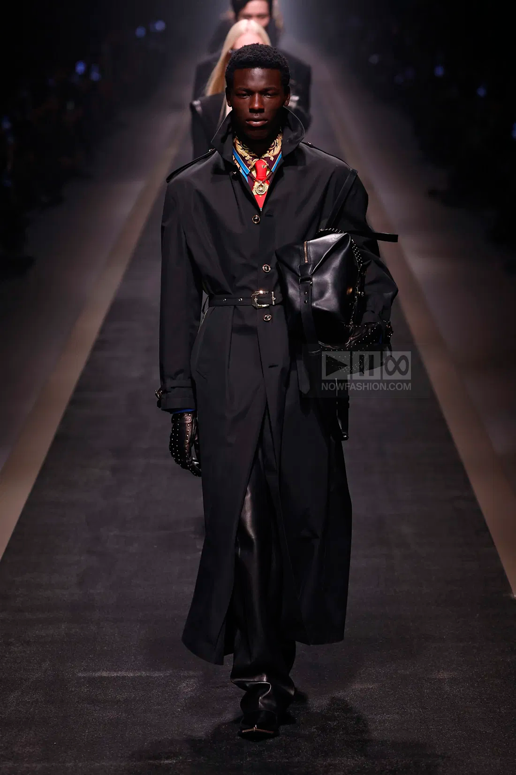 Male model wearing a black belted coat with leather gloves and accessories on the Versace Fall Winter 2025 Milan runway