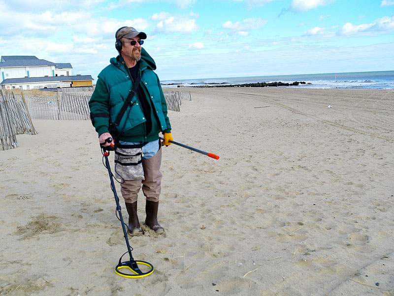 Person using a metal detector on a French beach, illustrating the practice of beach metal detecting relevant to legal and ethical discussions