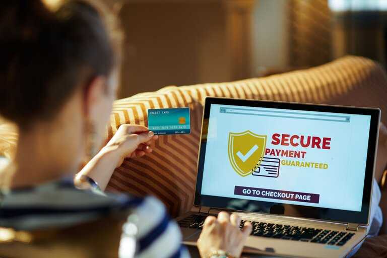 Person holding a credit card and using a laptop with a secure payment guaranteed message on the screen