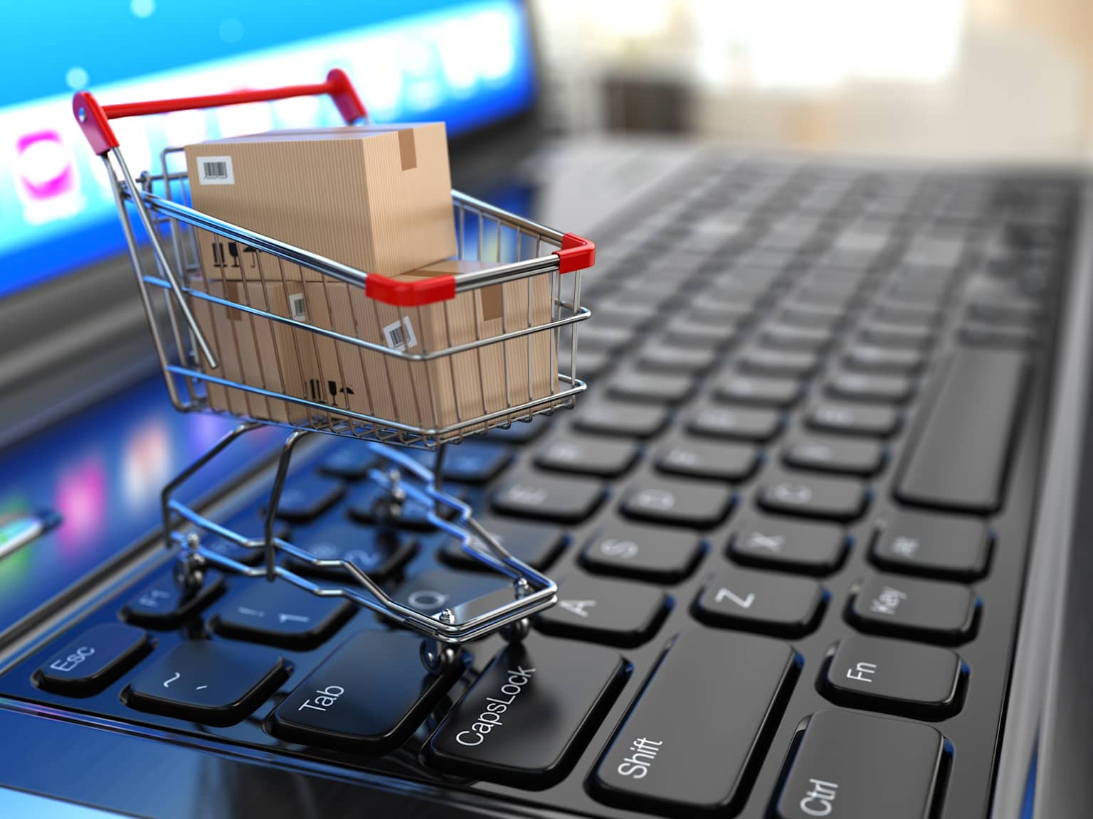Miniature shopping cart with boxes on a laptop keyboard symbolizing online e-commerce shopping